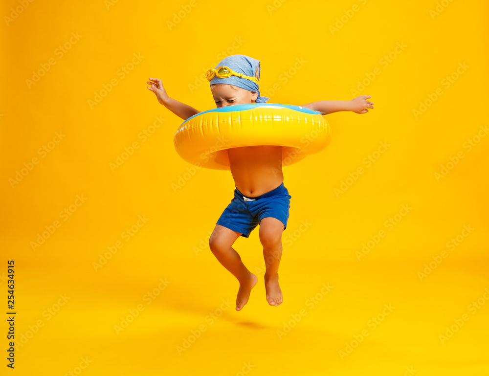 快乐的小男孩，穿着黄色背景的游泳圈甜甜圈泳衣。