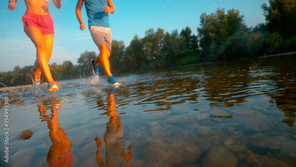 低角度：无法辨认的训练伙伴在宁静的河流中奔跑。