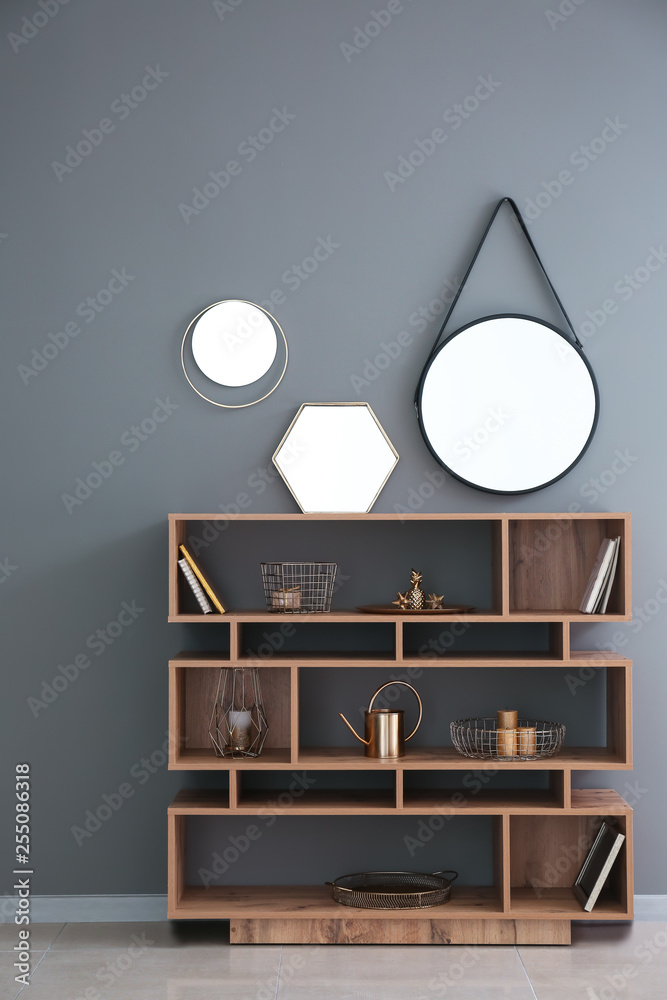 Wooden shelving unit with golden decor and mirrors on grey wall