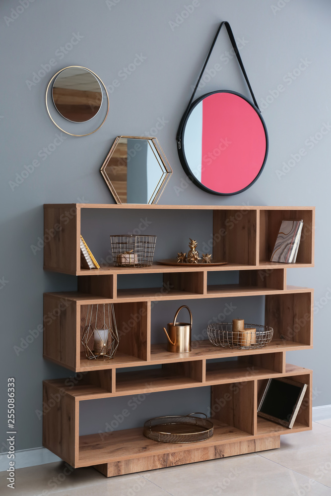 Wooden shelving unit with golden decor and mirrors on grey wall