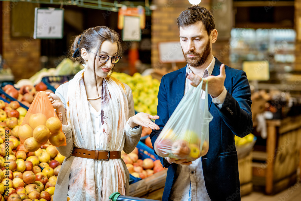 超市里用环保袋和塑料袋购买食物的男人和女人。环保袋的使用概念