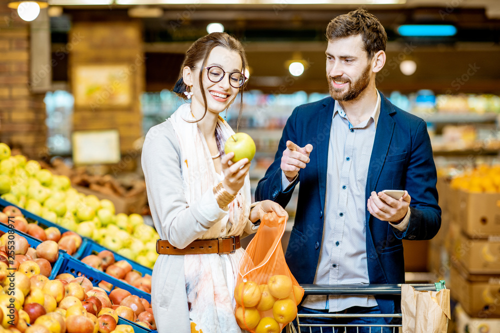年轻幸福的一对夫妇站在购物车旁购买新鲜水果和蔬菜