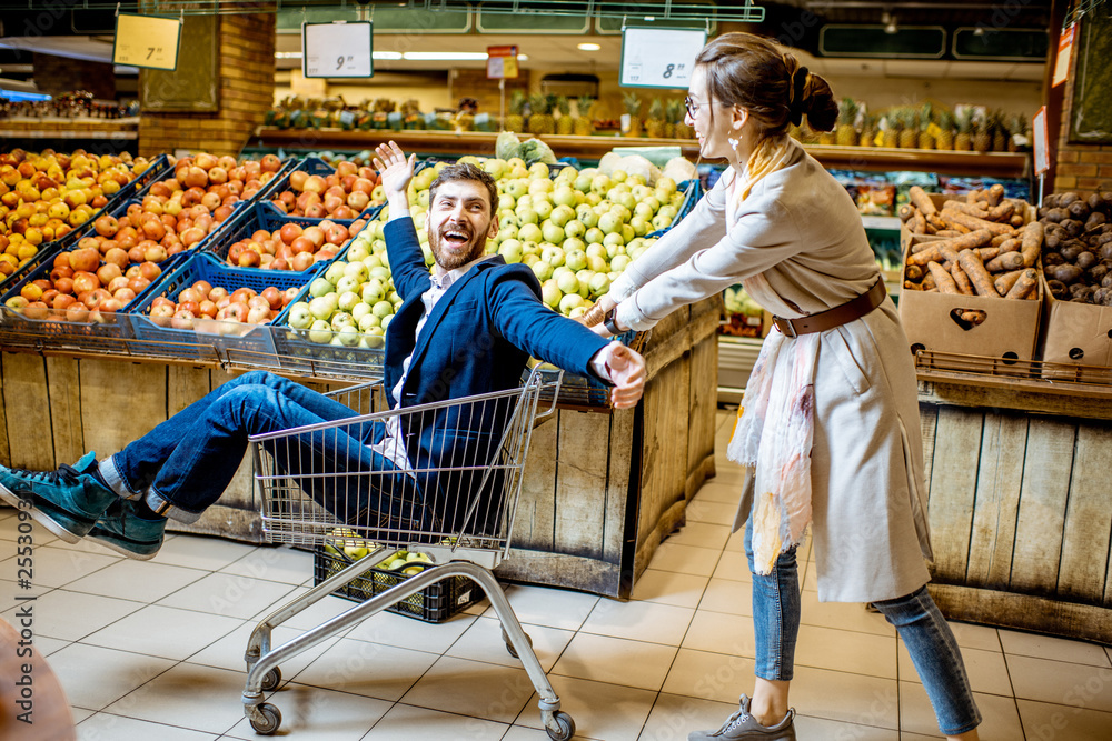 一男一女在超市里用购物车载着水果和蔬菜玩得很开心