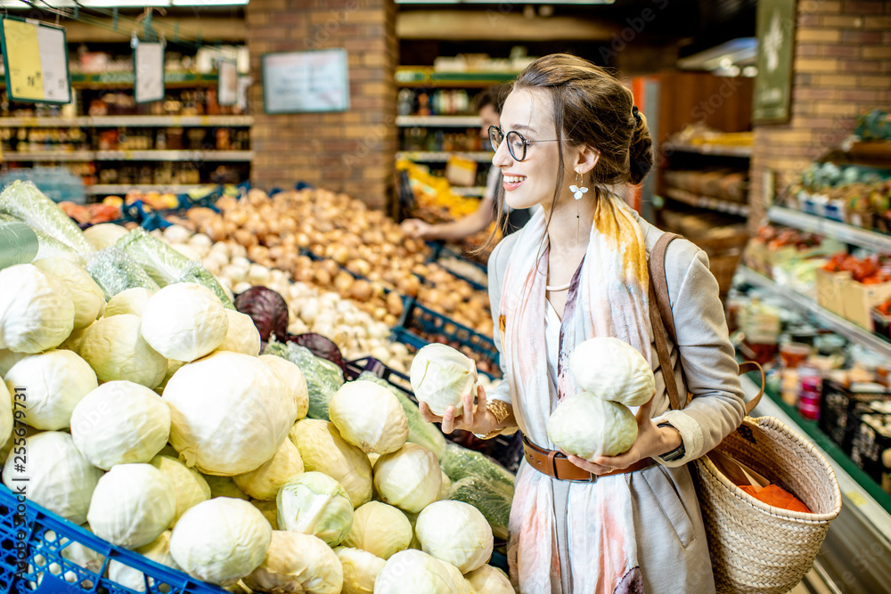 年轻女子站在超市蔬菜部选购卷心菜