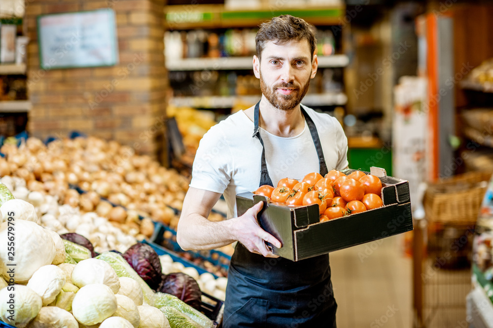 Portrait of a handsome shop worker or farmer holding box with fresh tomatoes in the vegetable depart