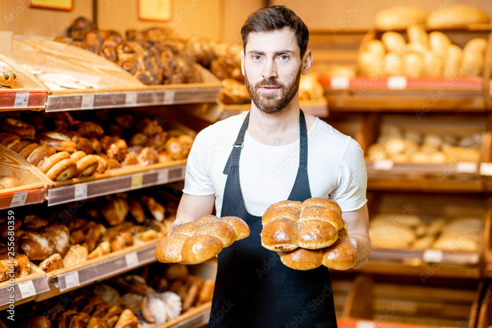 一位英俊的面包师穿着制服，拿着新鲜糕点站在面包店的画像