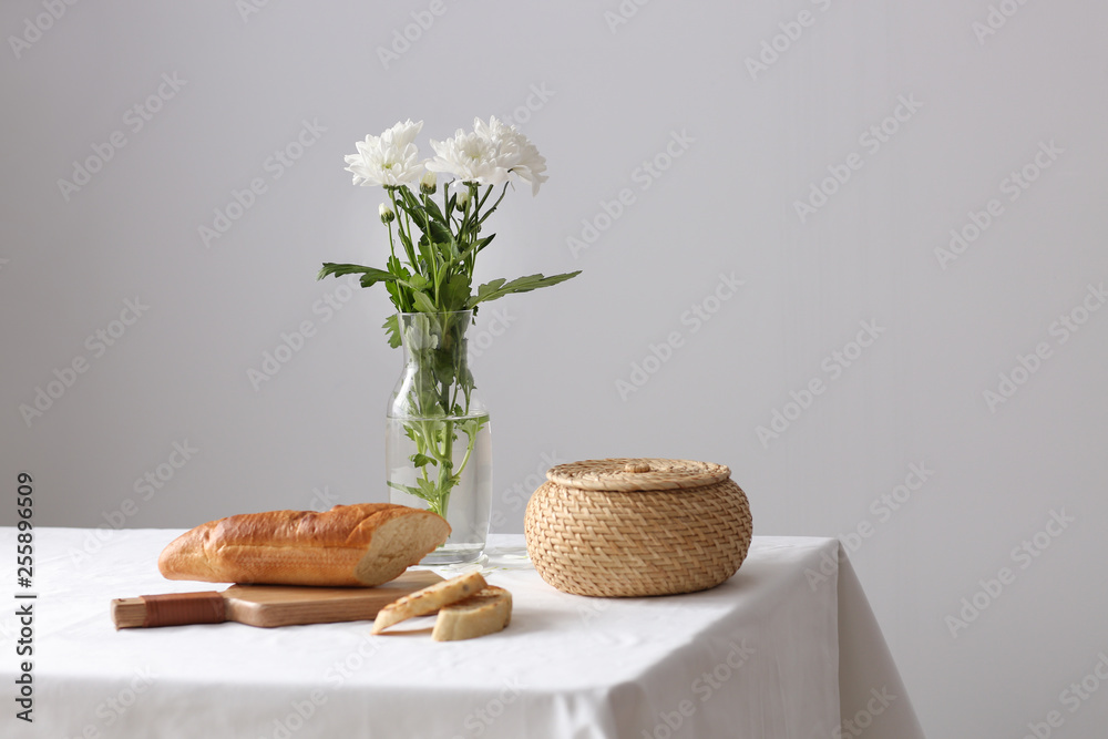 灰色背景下，桌子上花瓶里有美味面包和鲜花的砧板