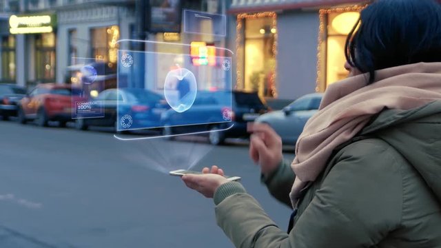 Unrecognizable woman standing on the street interacts HUD hologram with apple. Girl in warm clothes with a scarf uses technology of the future mobile screen on background of night city