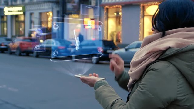Unrecognizable woman standing on the street interacts HUD hologram with electric guitar. Girl in warm clothes with a scarf uses technology of the future mobile screen on background of night city