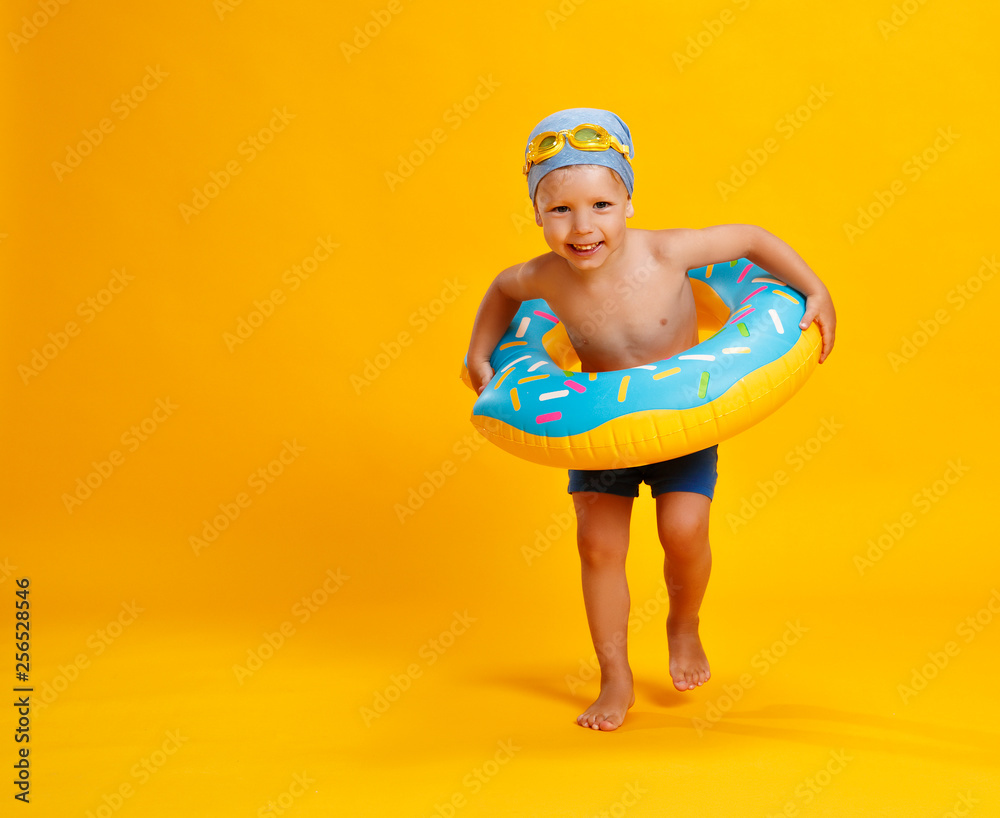 快乐的小男孩，穿着黄色背景的游泳圈甜甜圈泳衣。