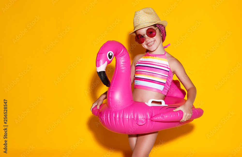 happy child girl in swimsuit with swimming ring flamingo on colored yellow background