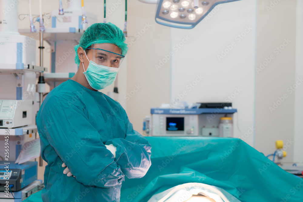 亚洲微笑的外科医生站在医院的手术室里交叉双臂。