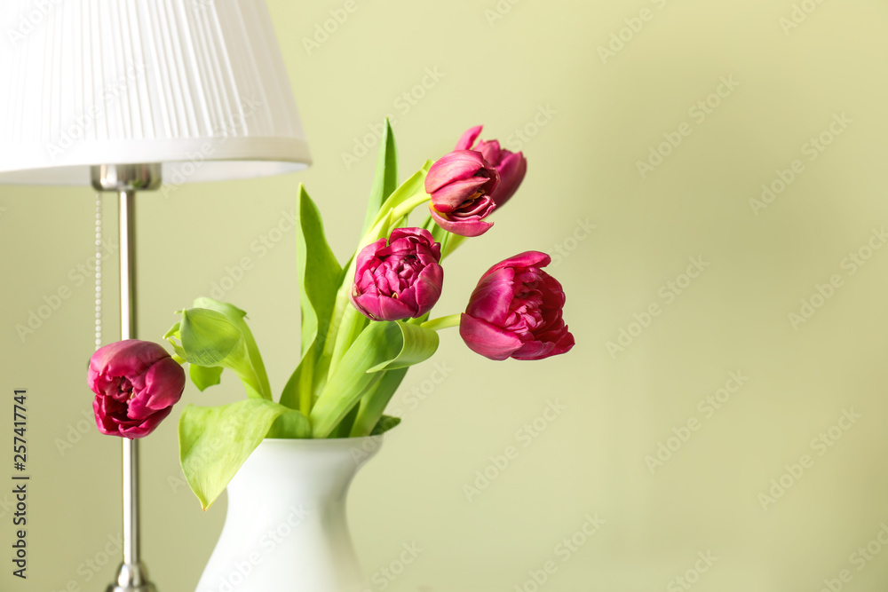 Beautiful tulips in vase with lamp on color background