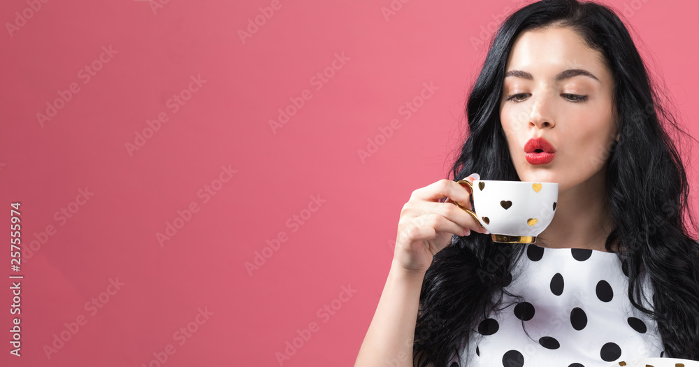 Young woman drinking coffee on a solid background