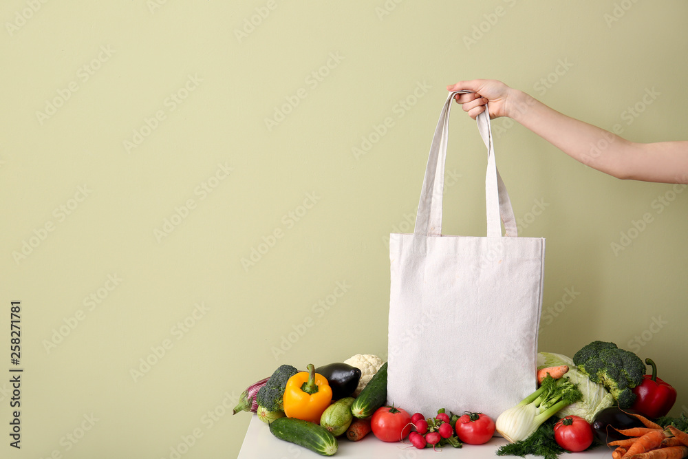 女性手拿环保袋，桌上有新鲜蔬菜，背景为彩色
