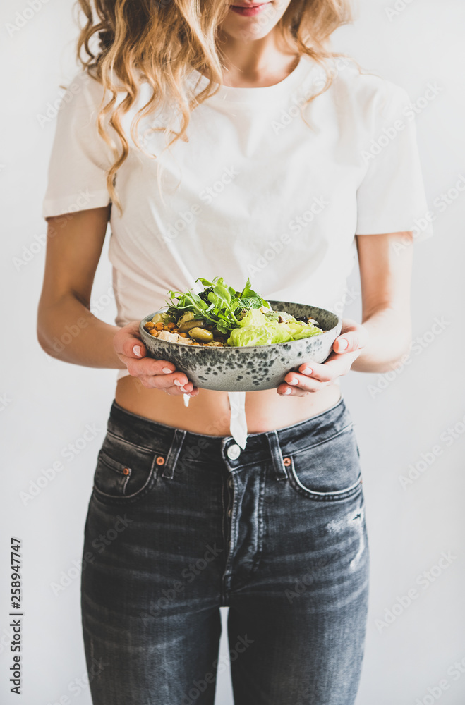 Healthy dinner, lunch. Woman in jeans standing and holding vegan superbowl or Buddha bowl with hummu