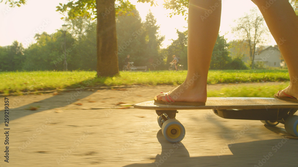 LENS FLARE：阳光明媚的春天，穿着人字拖的运动女孩在公园里滑冰。