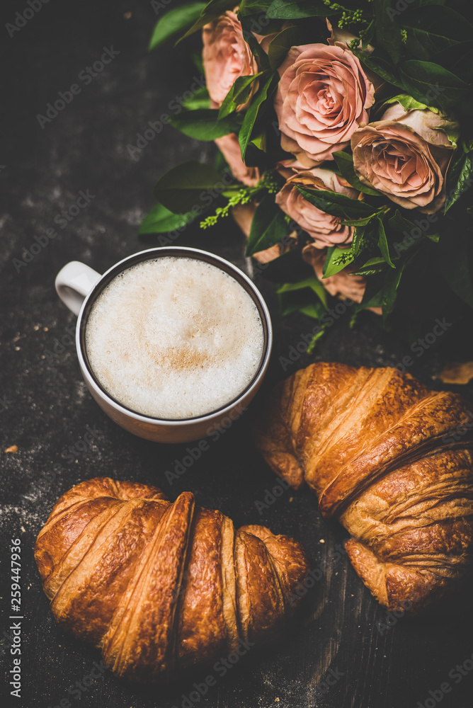 咖啡休息时间。一杯热卡布奇诺，配新鲜羊角面包和一束粉色花朵。