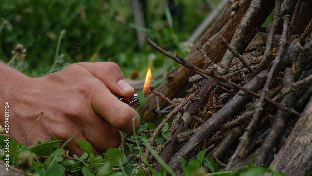 MACRO: Man holding a lighter tries to ignite a campfire during a camping trip.