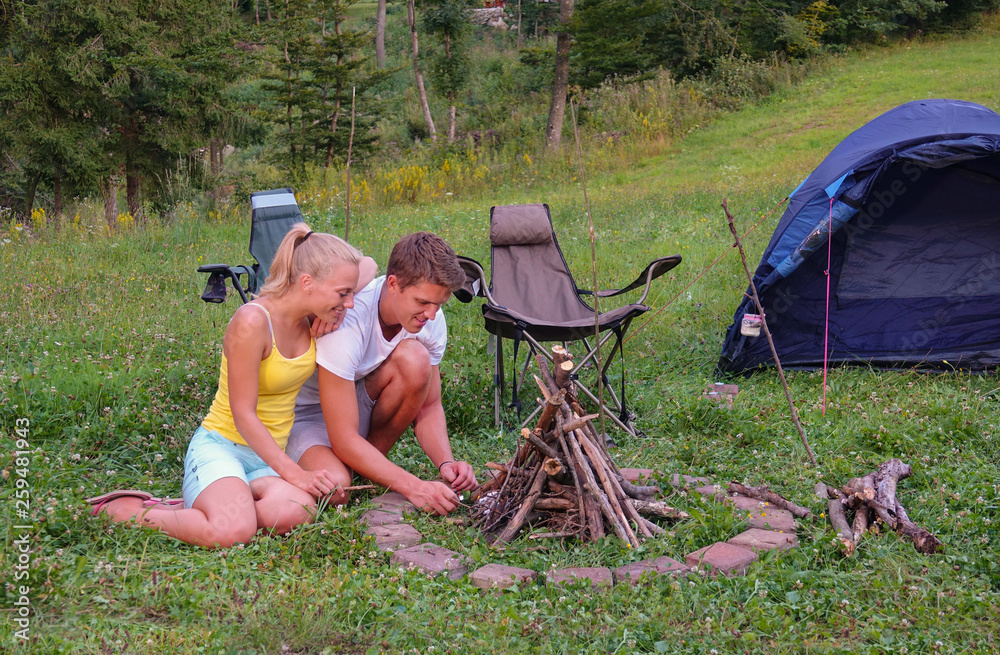 Happy tourist couple kneel by the fire pit as they try to light a campfire.