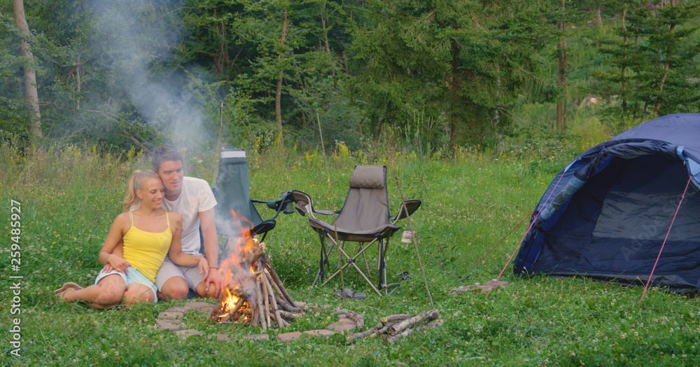 复制空间：一对可爱的情侣在夏季露营旅行中拥抱在噼啪作响的炉火旁。