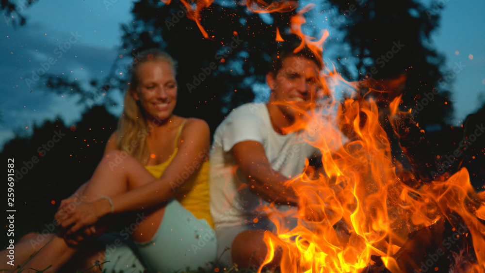 特写：当一对游客夫妇坐在附近时，篝火里冒出火花。