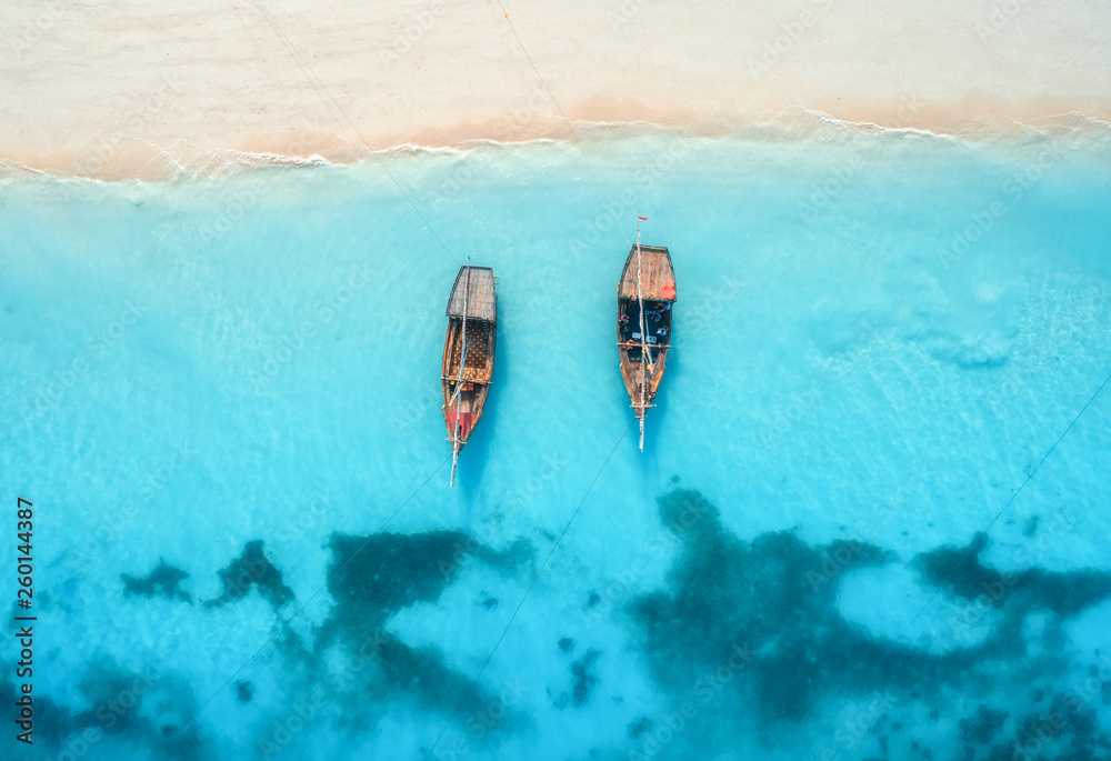 Aerial view of the fishing boats in clear blue water at sunset in summer. Top view from drone of boa