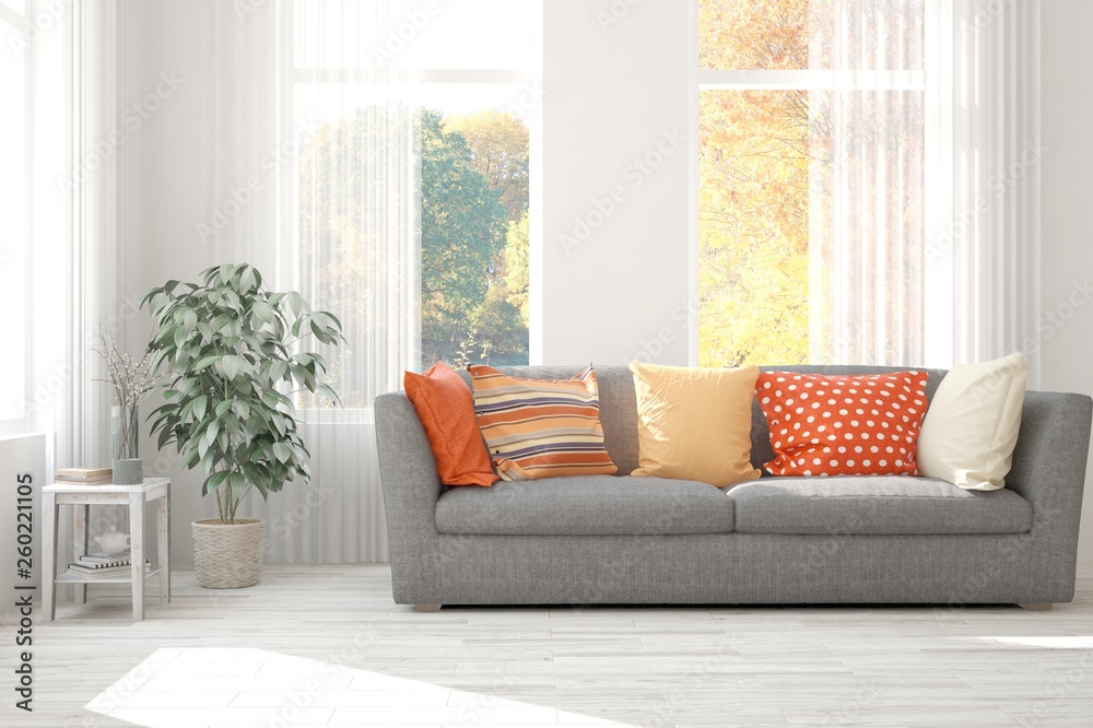 白色时尚的极简主义房间，带沙发，窗户里有秋天的风景。斯堪的纳维亚室内设计