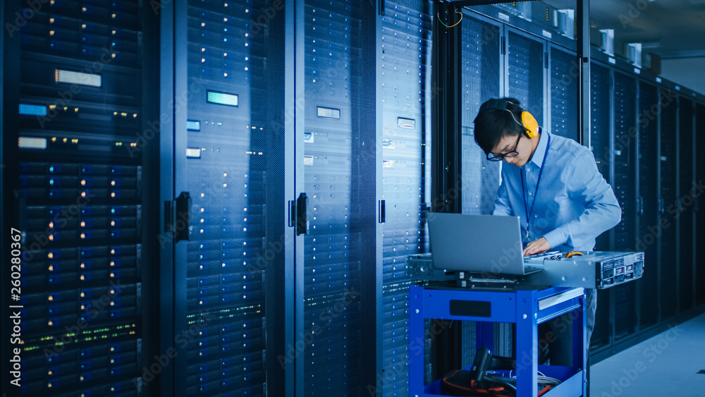 In the Modern Data Center: IT Technician Wearing Protective Headphones Working with Server Racks, on