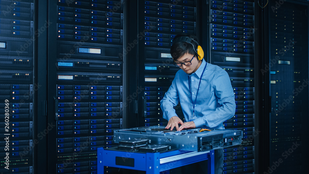 在现代数据中心：戴着防护耳机的IT技术人员在服务器机架上工作