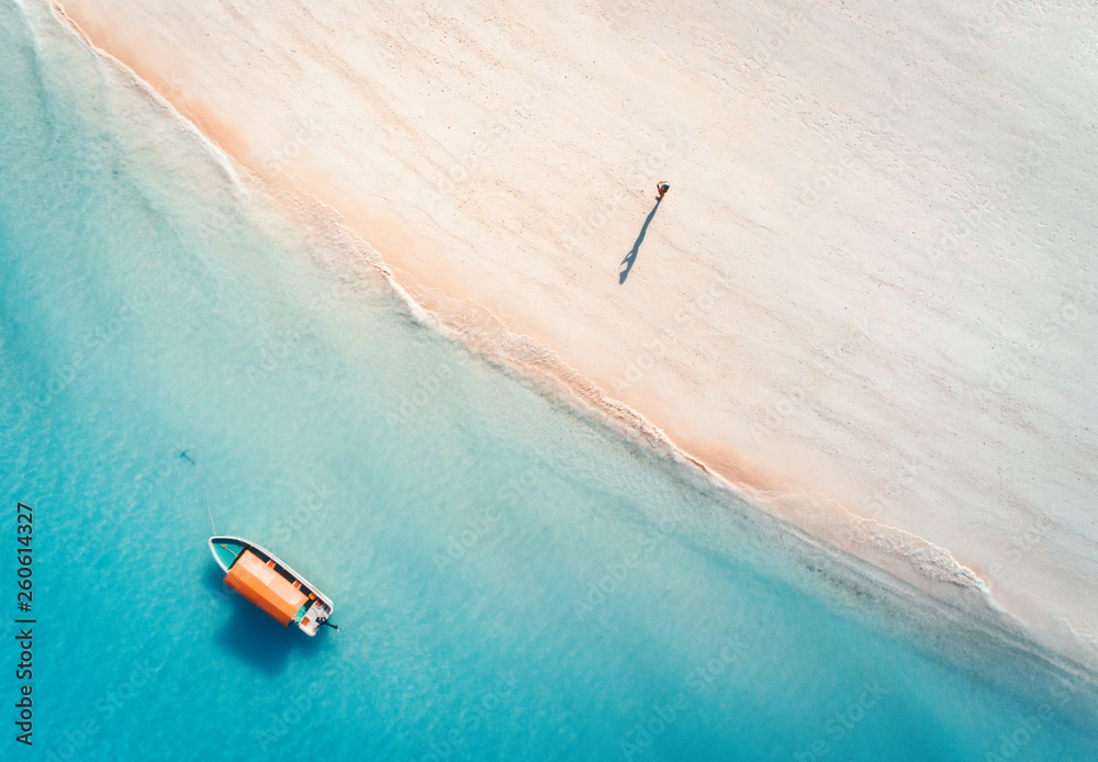 夏日日落时，蓝色海水中的渔船和沙滩上的人的鸟瞰图。
