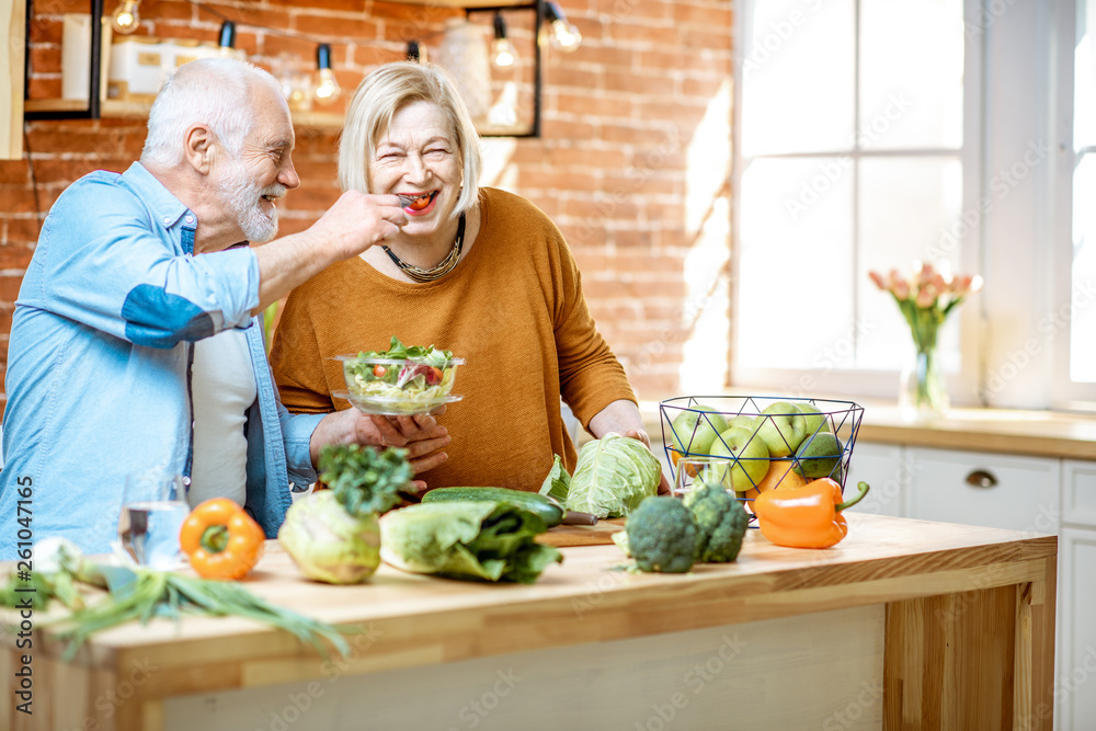 快乐的老年夫妇站在家里的厨房里吃沙拉和健康的食物。海螺