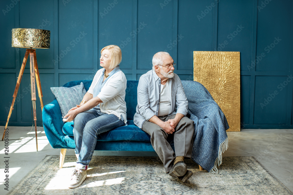 Offended senior man and woman feeling sad, sitting back to each other on the couch at home