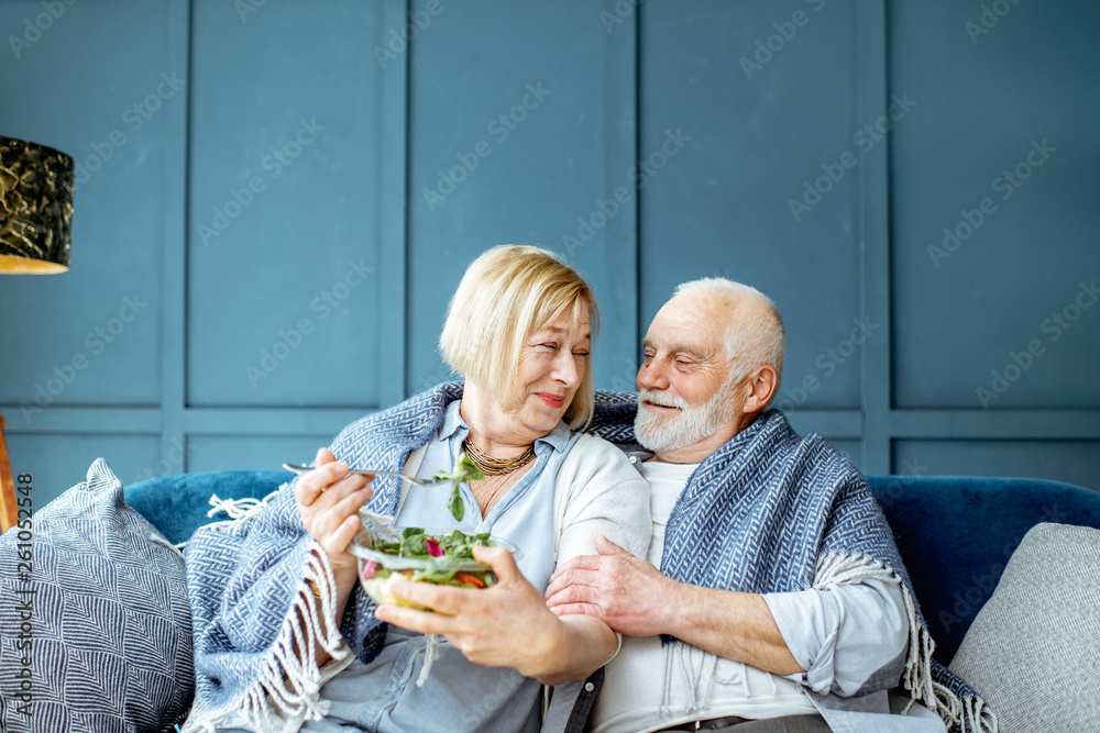 可爱的老年夫妇裹着格子布坐在家里的沙发上吃着健康的沙拉