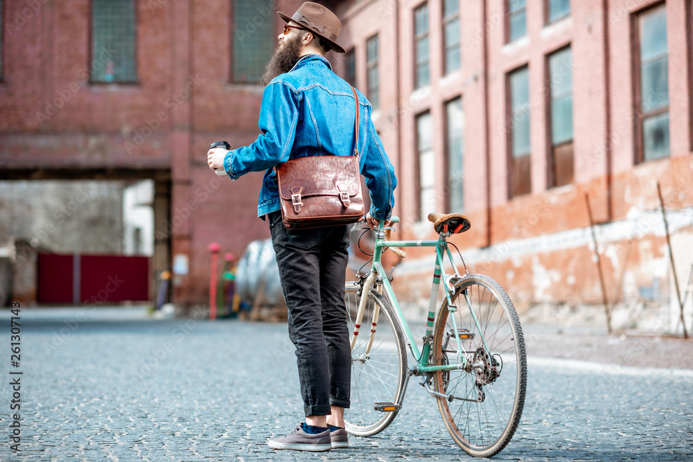 时尚潮人在工业城市背景下，带着咖啡和复古自行车行走，后景