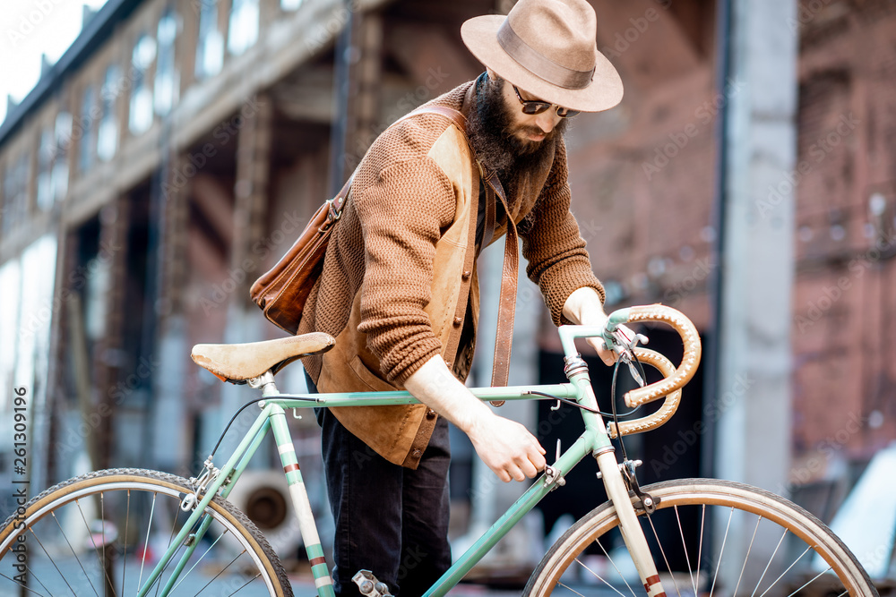 留胡子的潮人穿着时髦，戴着帽子，在城市的乡间小路上骑着复古自行车站着