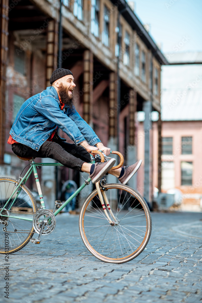 Stylish man as a crazy hipster having fun, riding retro bicycle outdoors on the industrial urban bac