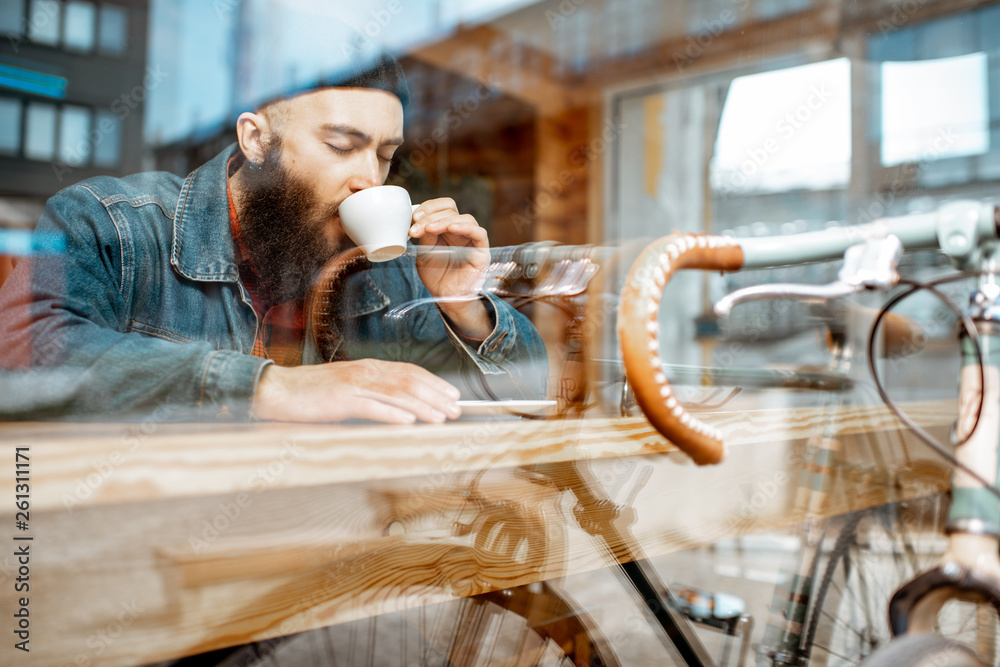 时尚男子骑着复古自行车坐在靠窗的咖啡馆里喝咖啡。Vi