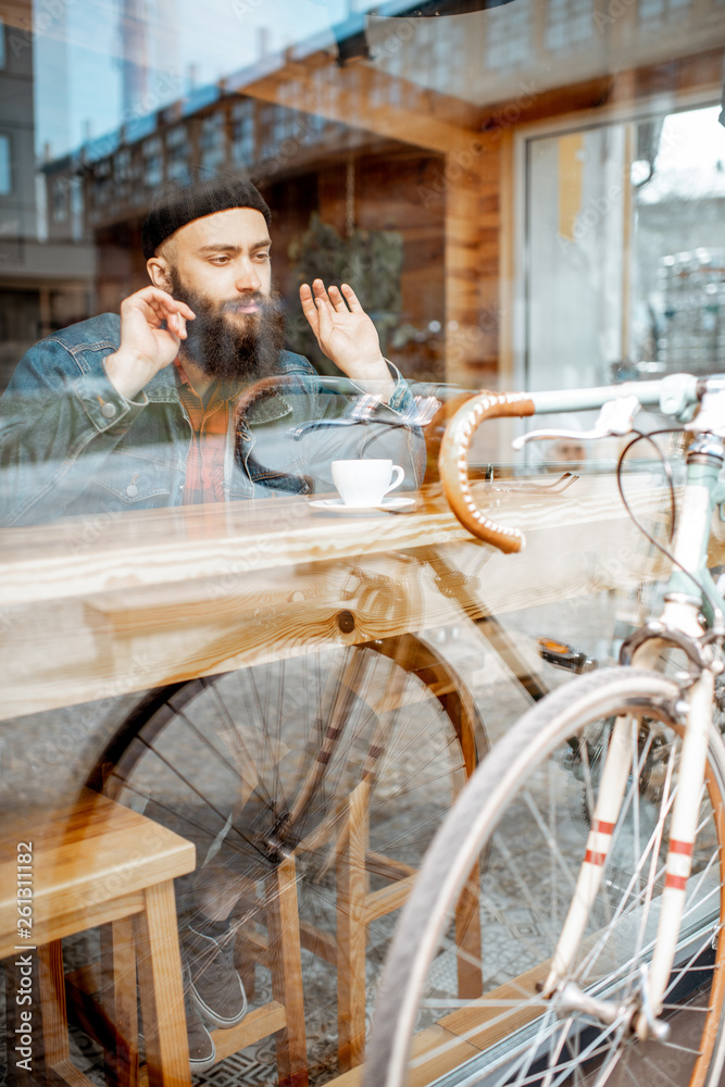 时髦的男人骑着复古自行车坐在靠窗的咖啡馆里喝咖啡。宽