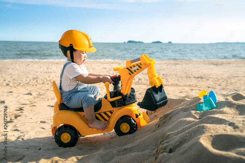 亚洲男孩在海滩上玩挖掘机玩具