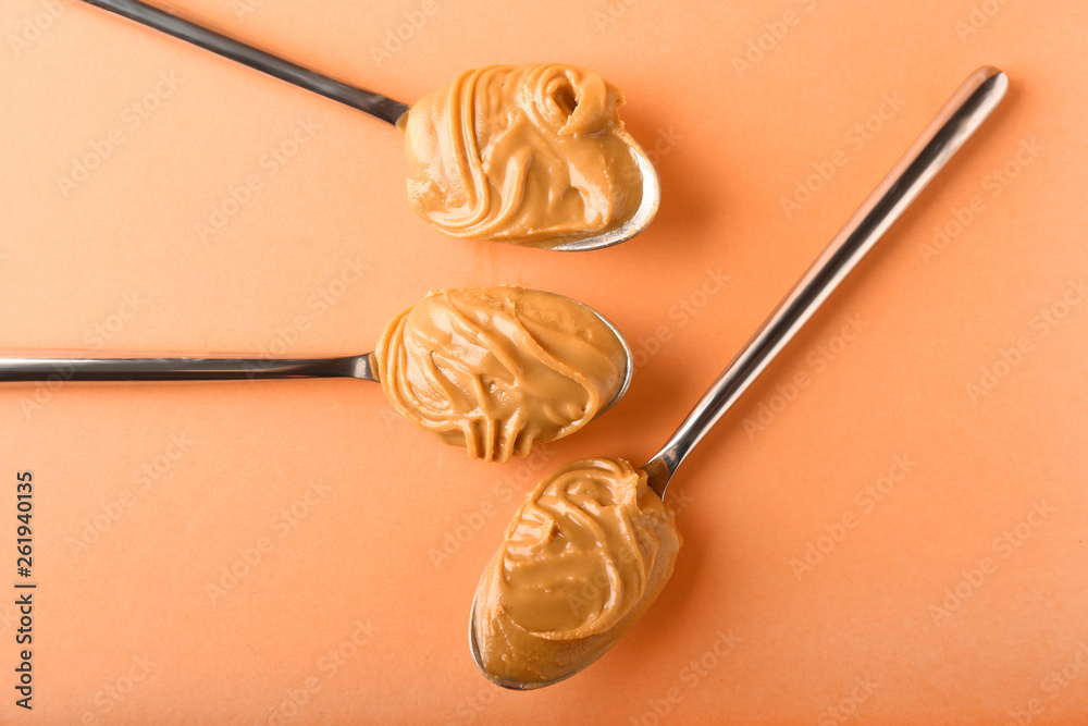 Spoons with peanut butter on color background