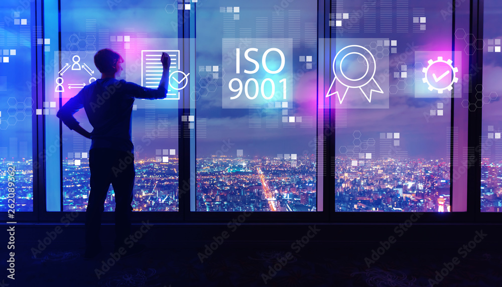 ISO 9001 with man writing on large windows high above a sprawling city at night