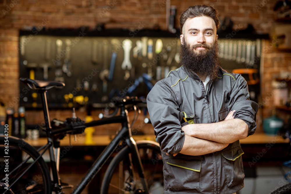 Portrait of a handsome bearded repairman in workwear at the bicycle workshop