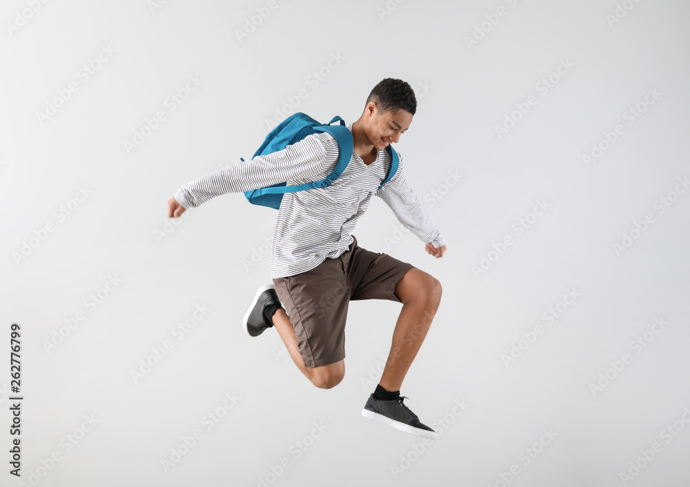 Portrait of jumping African-American teenage boy on grey background