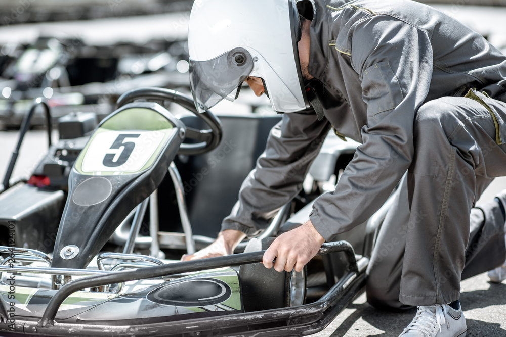 Racer or repairman in uniform serving go-kart machine before racing on the track