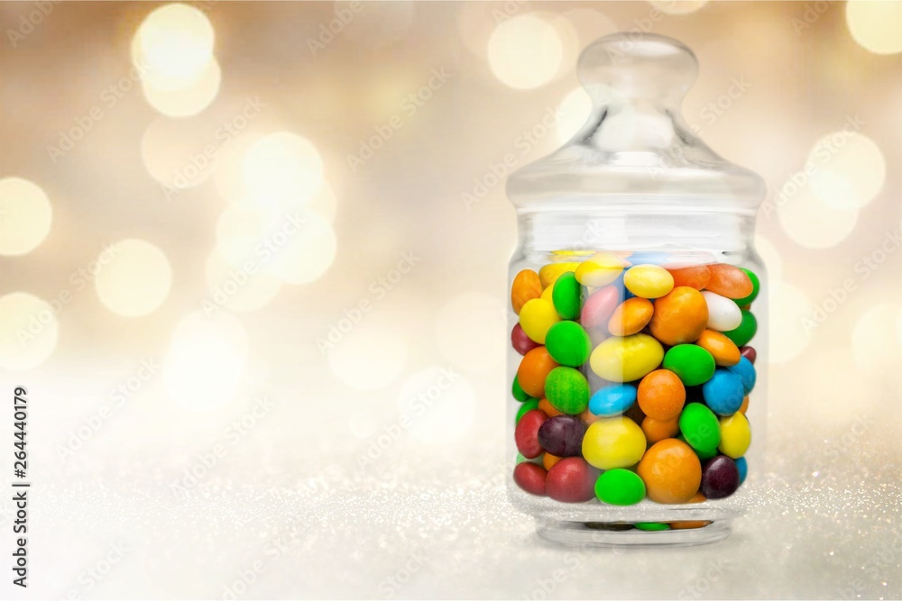 Transparent glass jar with colorful chocolate candies on table