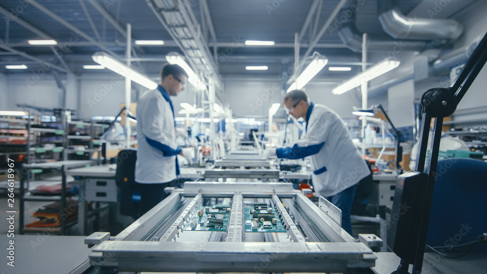 Shot of an Electronics Factory Workers Assembling Circuit Boards by Hand While it Stands on the Asse