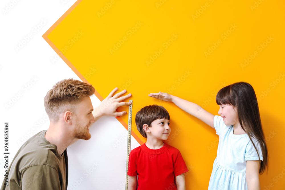 Father and his little children measuring height near wall