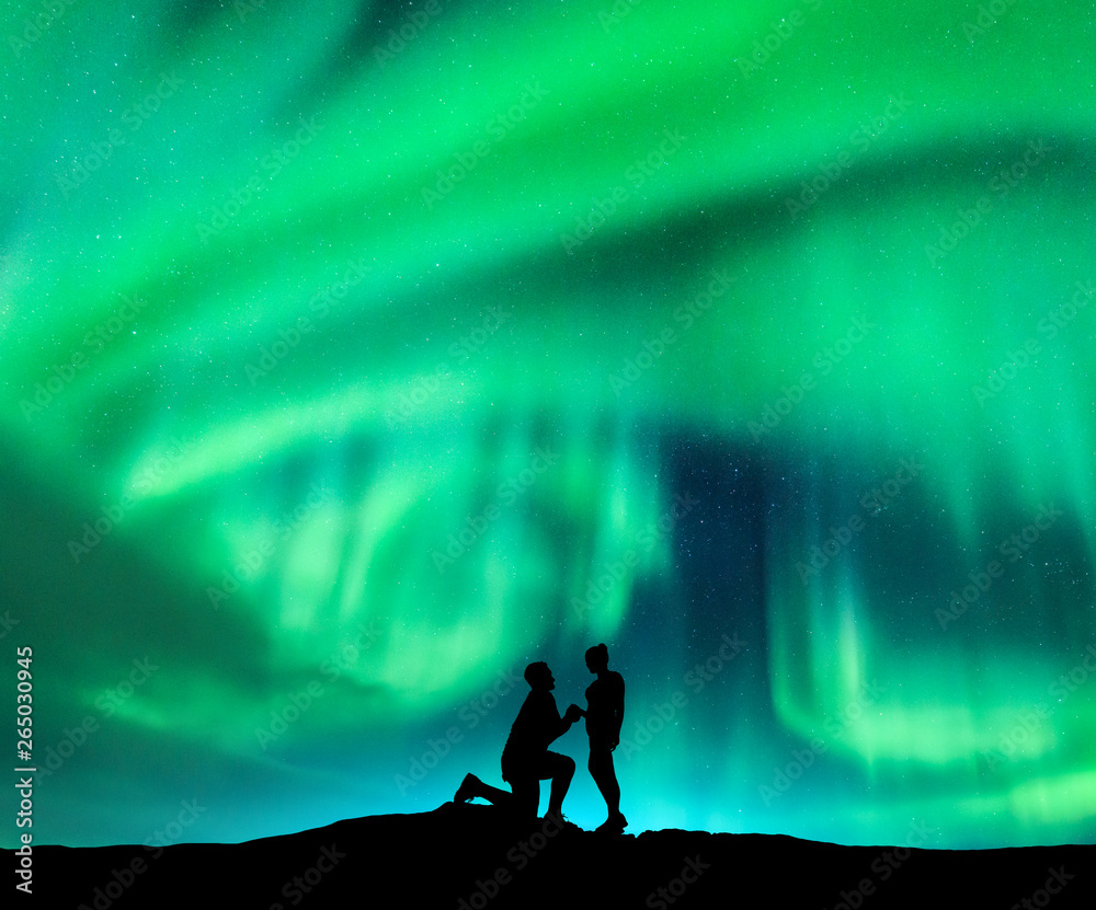 北极光和一个男人向女友求婚的剪影。夜景