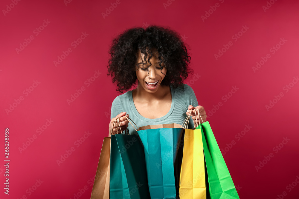 快乐的非裔美国女人看着彩色背景的购物袋